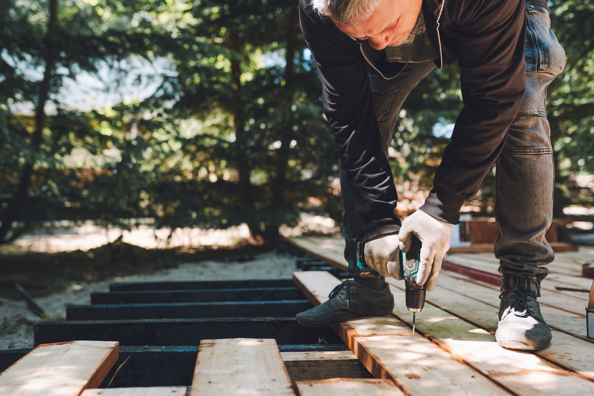 Construction worker using drill for wooden boards outdoors for foundation restoration.