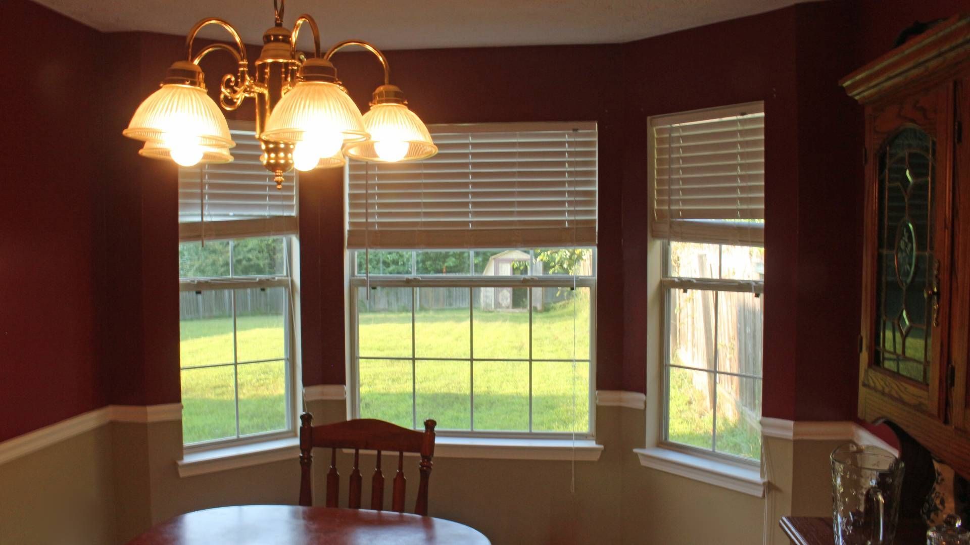 Bay window blinds in a dining room with ceiling lights on near at Harmony Blinds & Shutters near San