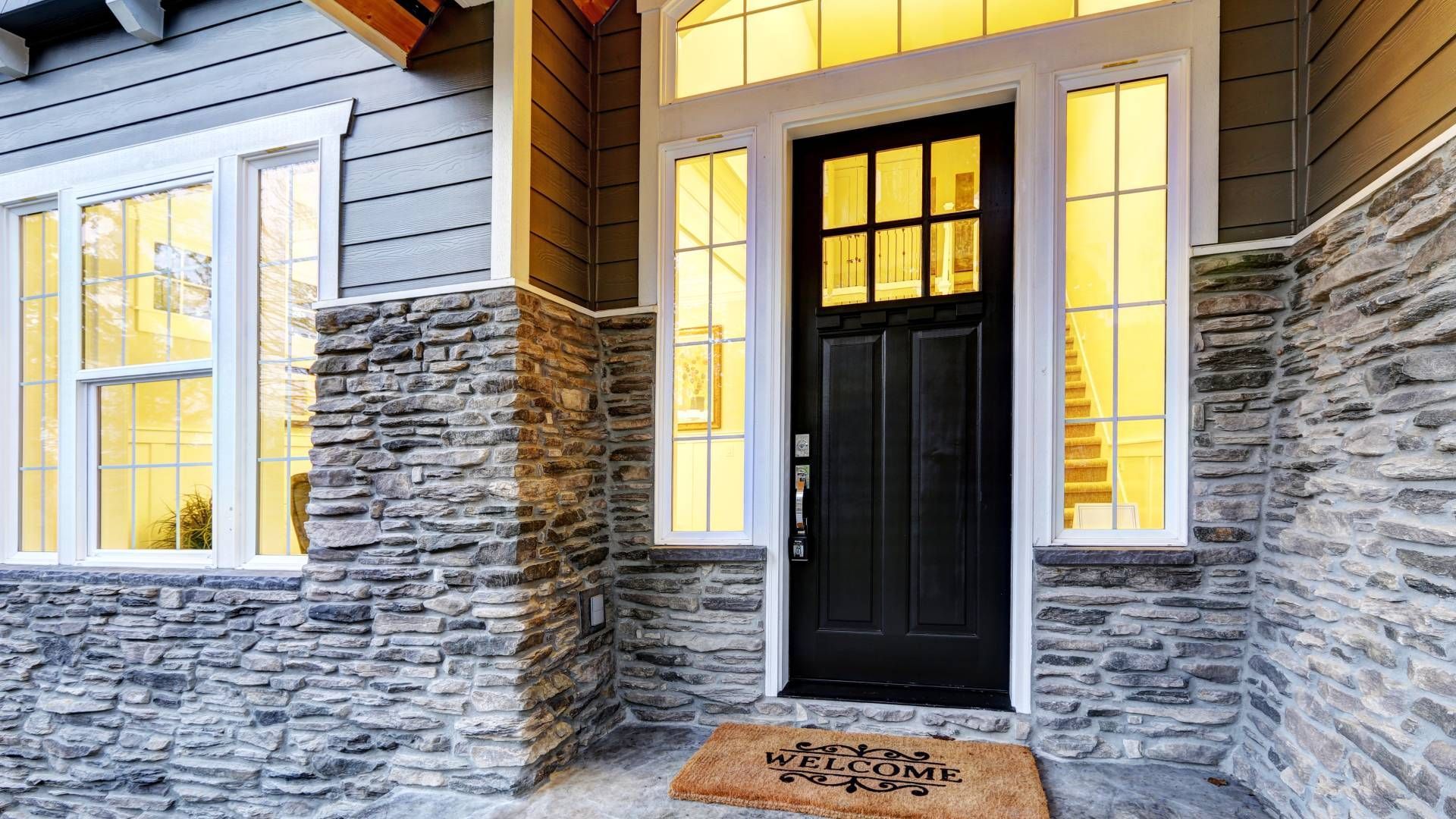 A residential home's exterior front door with sidelights that are lacking window blinds on them at H