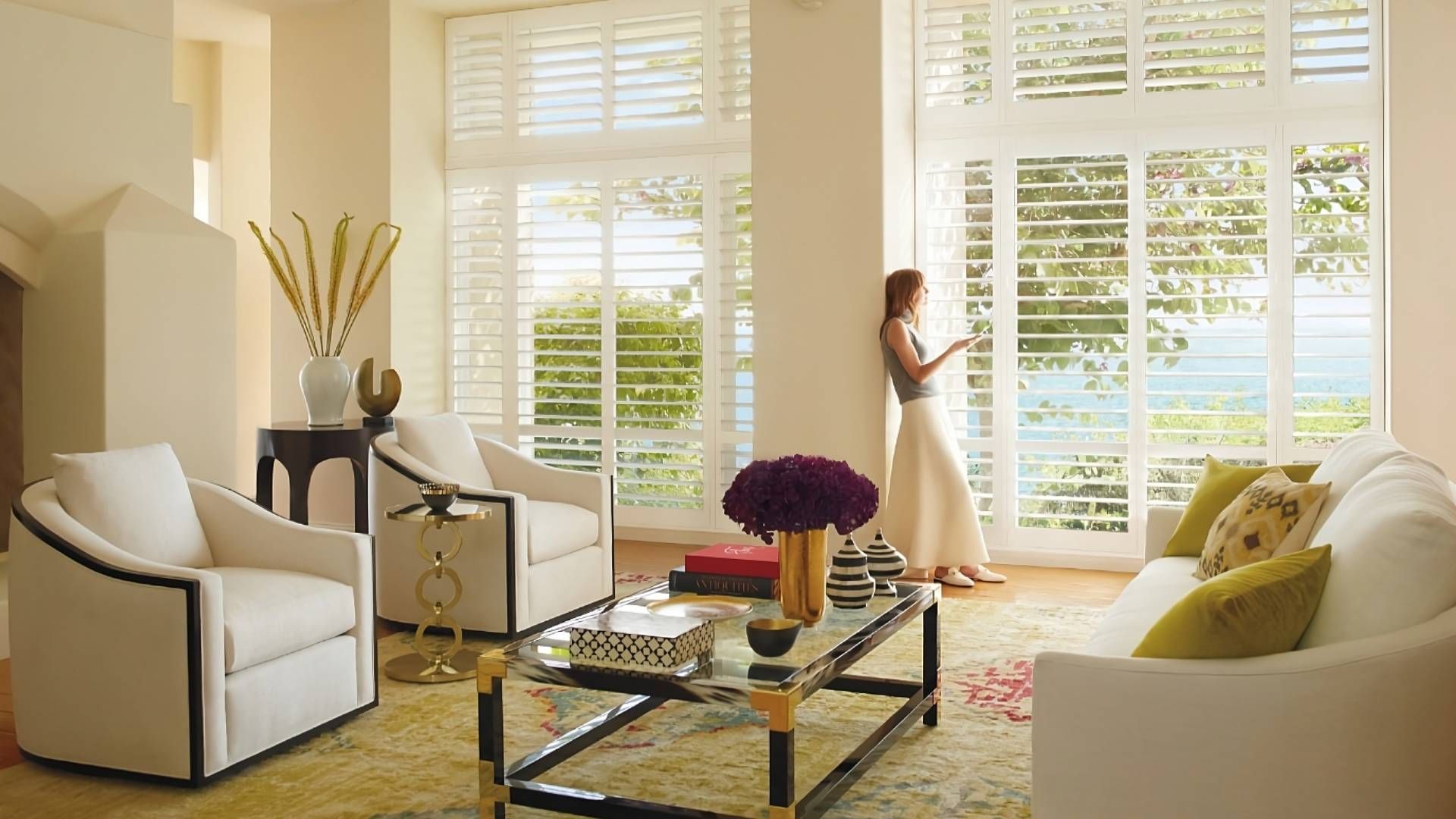 Hunter Douglas Palm Beach™ Polystain™ Vinyl Shutters as living room shades with a woman peering outs