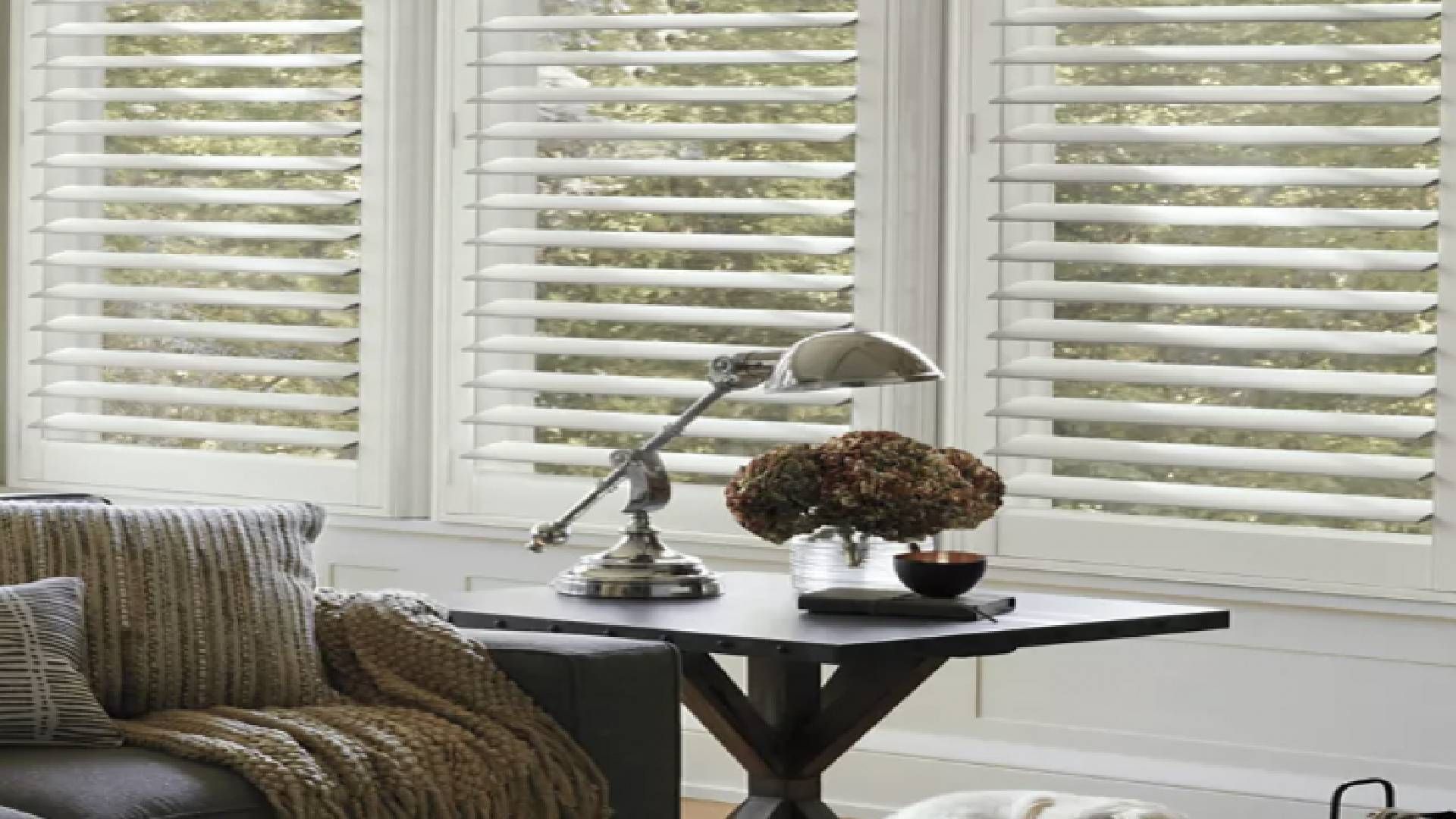 A table and sofa in a living room with large windows covered by NewStyle® Composite Shutters