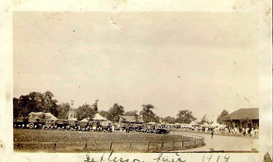 A sepia-toned vintage photo of a fairground with tents, people, and a wooden building, labeled 'Jefferson Fair 1884.'