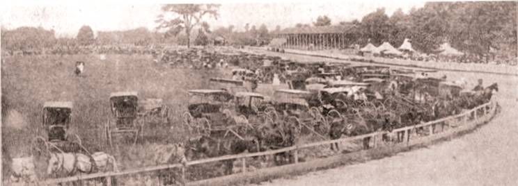 A vintage, sepia-toned photo of a large group of horse-drawn carriages parked in a line along a wooden fence.