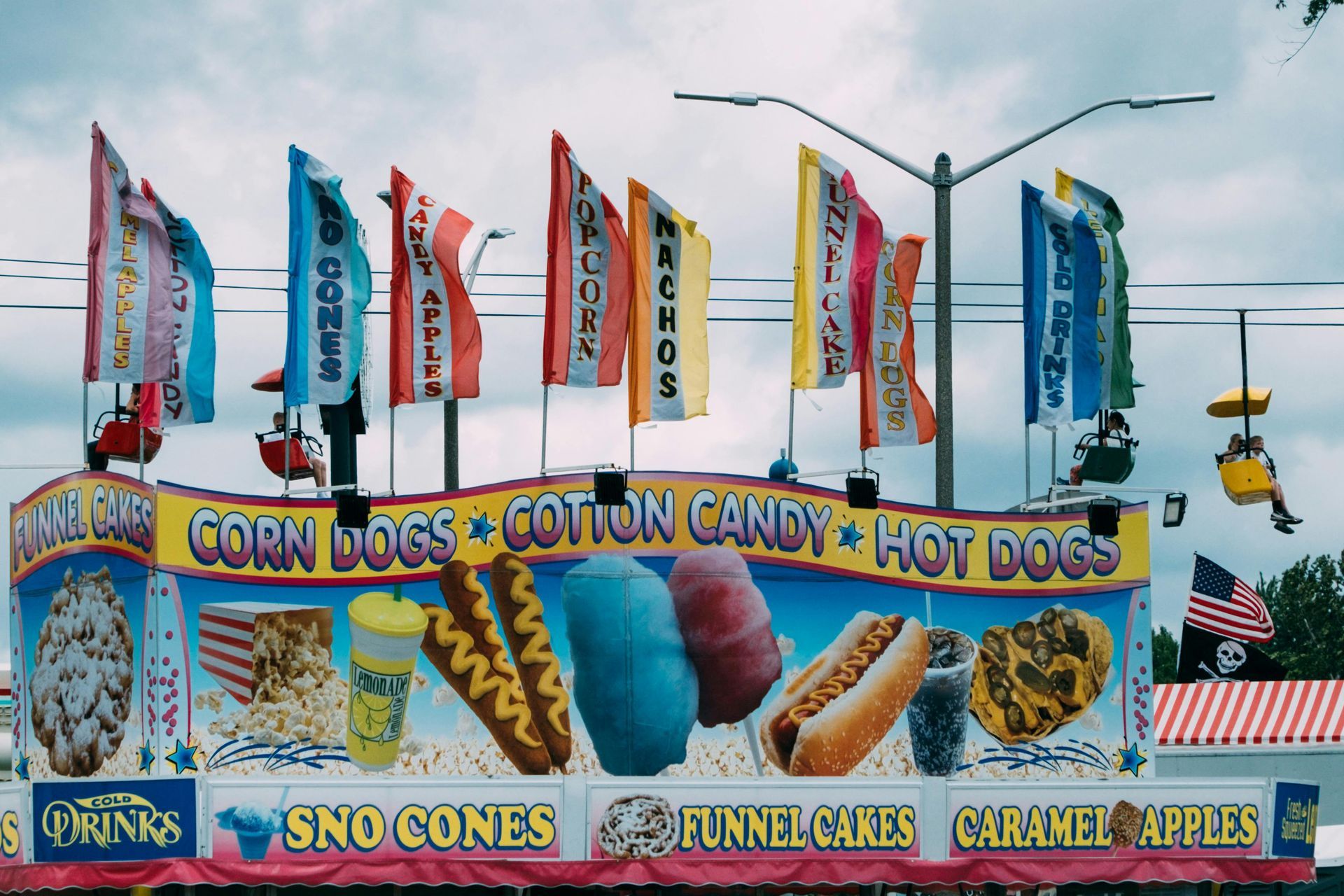 A colorful fair food stand displaying signs and illustrations for snacks like corn dogs, funnel cakes, and cotton candy.