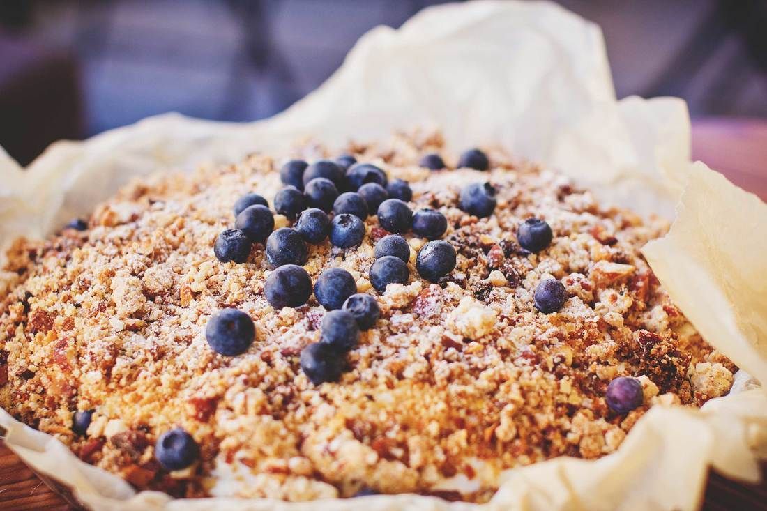 A blueberry crumble cake with a nutty, golden-brown crust sitting on crinkled parchment paper.