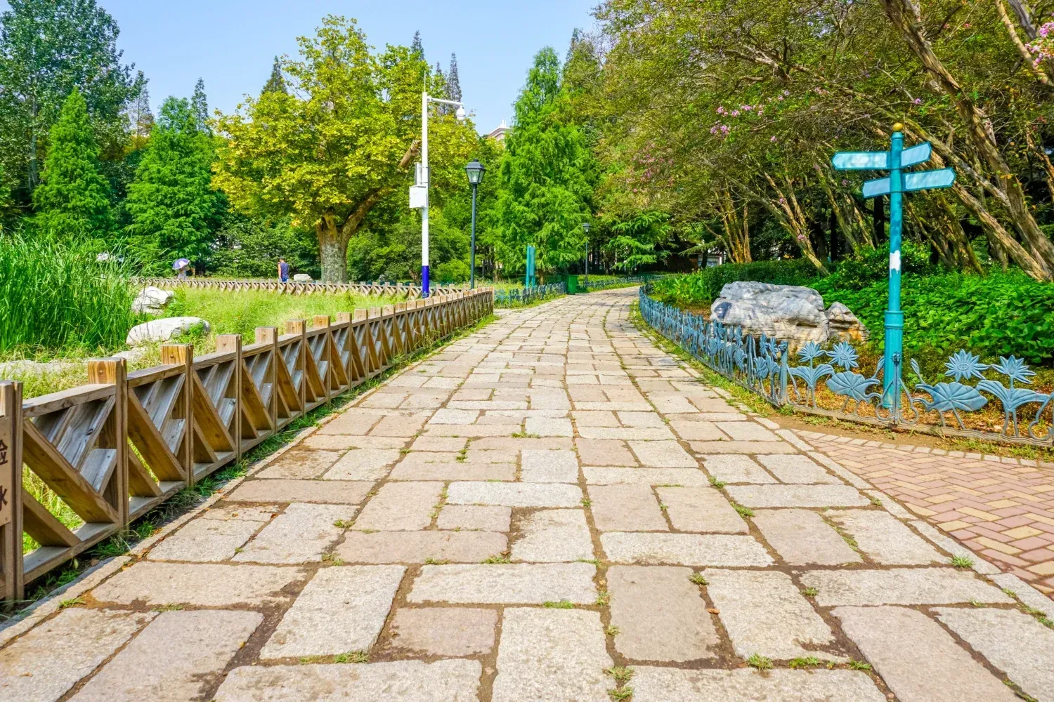 A brick walkway in a park with trees and a wooden fence.