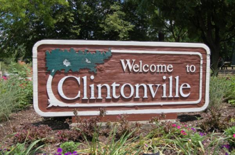 A welcome to clintonville sign is surrounded by flowers and trees.