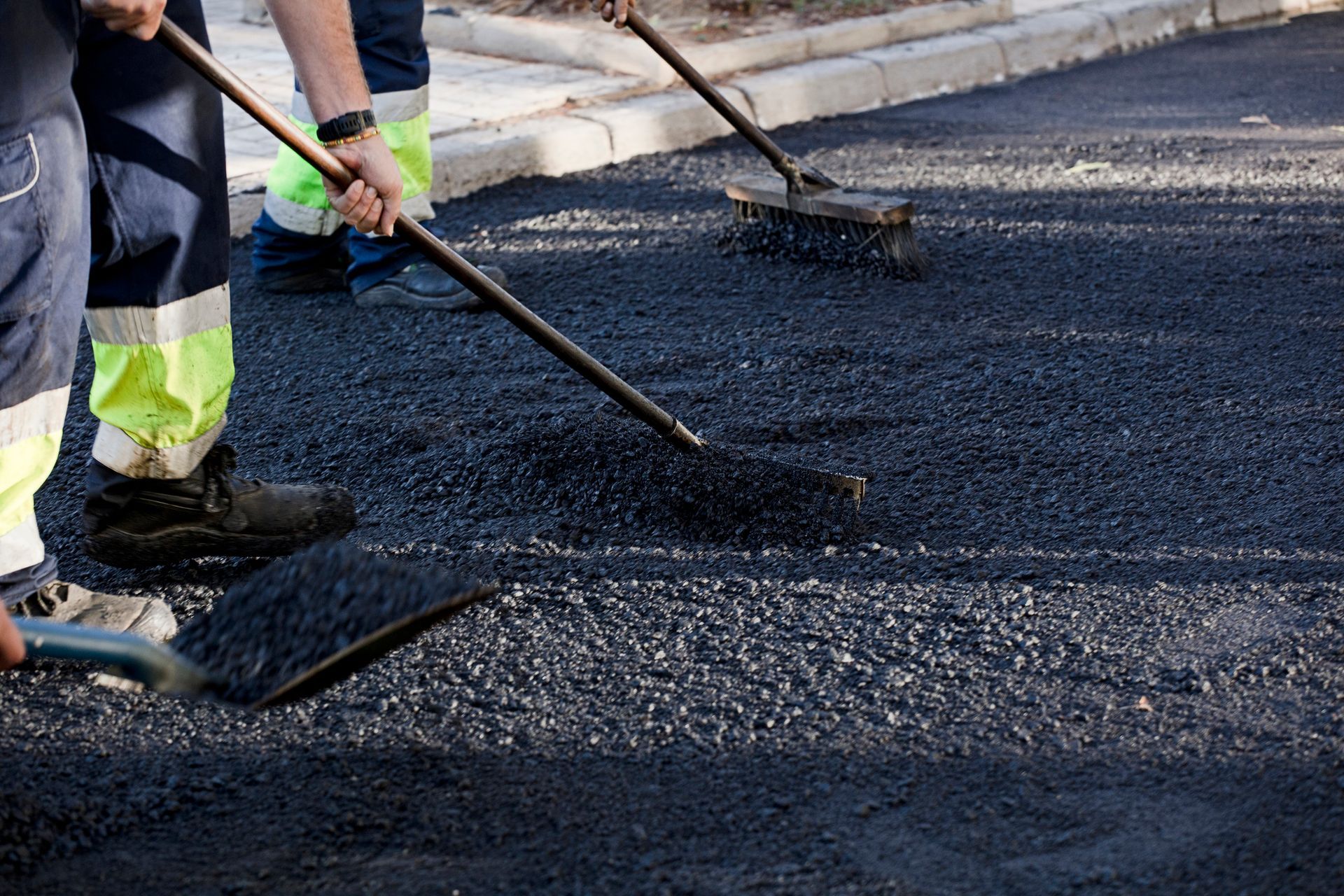 A man is spreading asphalt on the ground with a shovel and broom.
