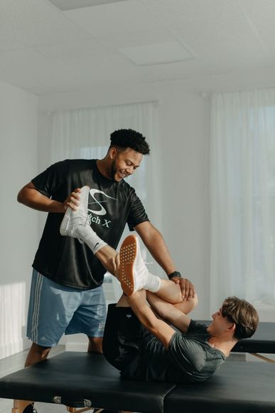 Physical therapist stretches a patient's leg in a light-filled room.