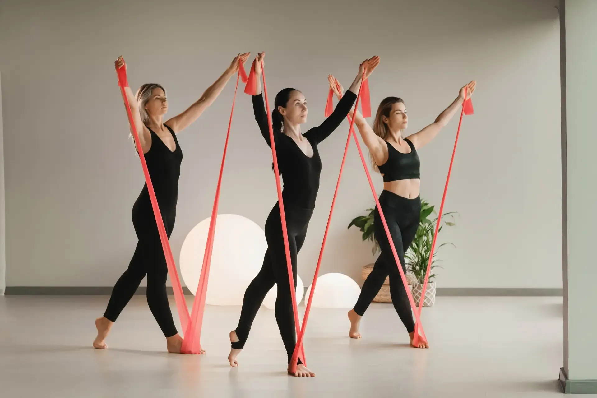 Three women wearing black suits are using a stretch band for daily exercise.