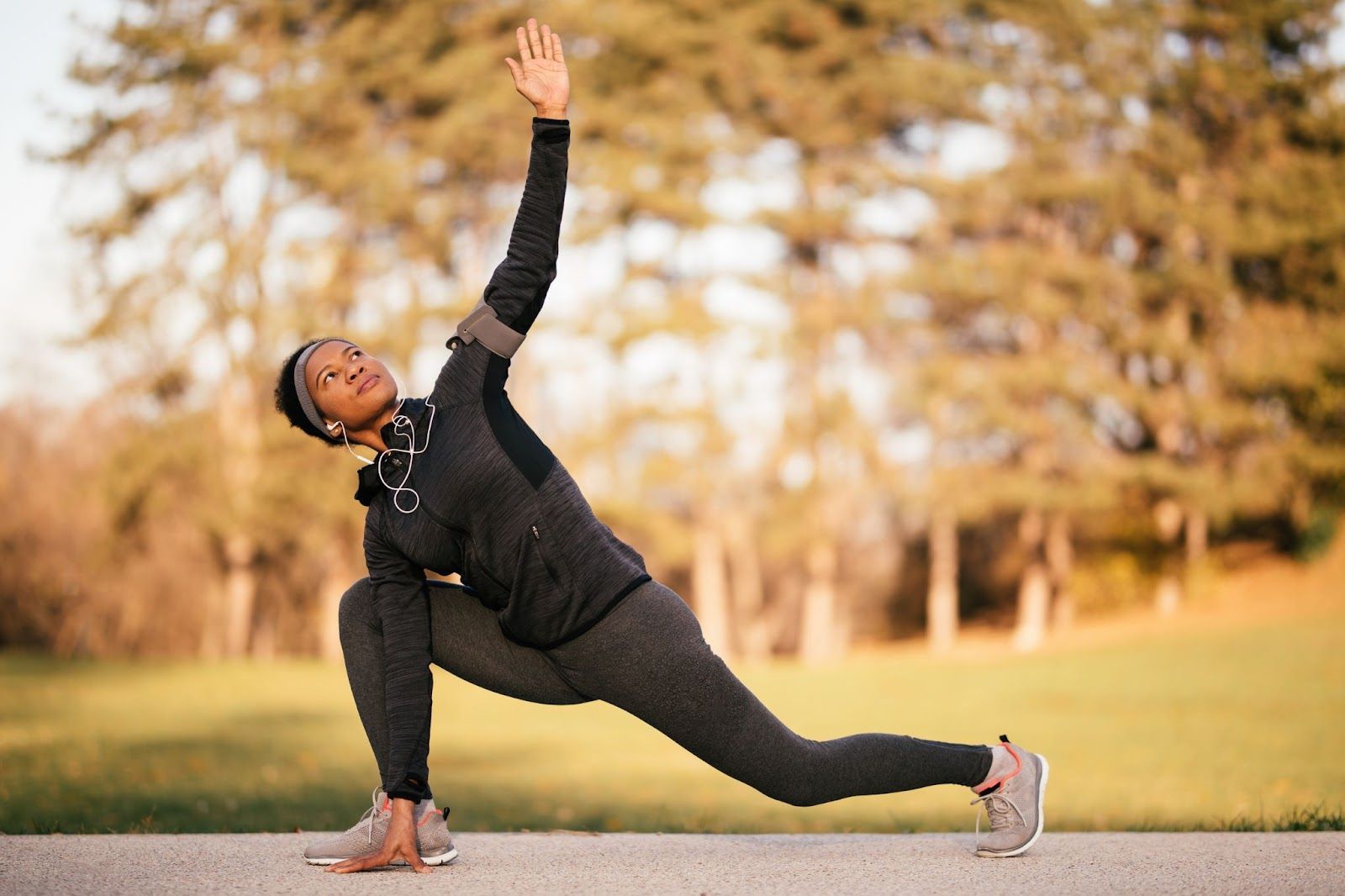 An African American woman in athletic gear performing stretching exercises in a park to warm up for 