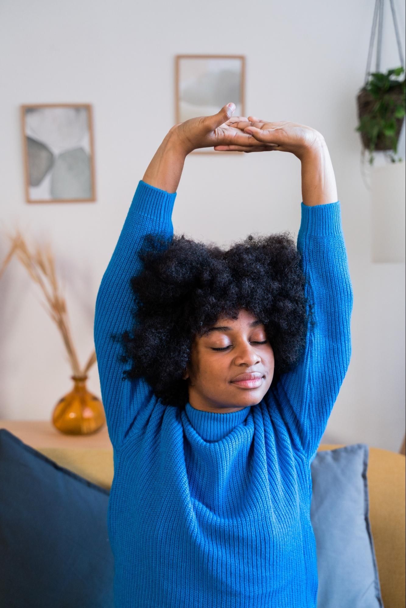 A young woman stretches at home with a relaxed look on her face. 