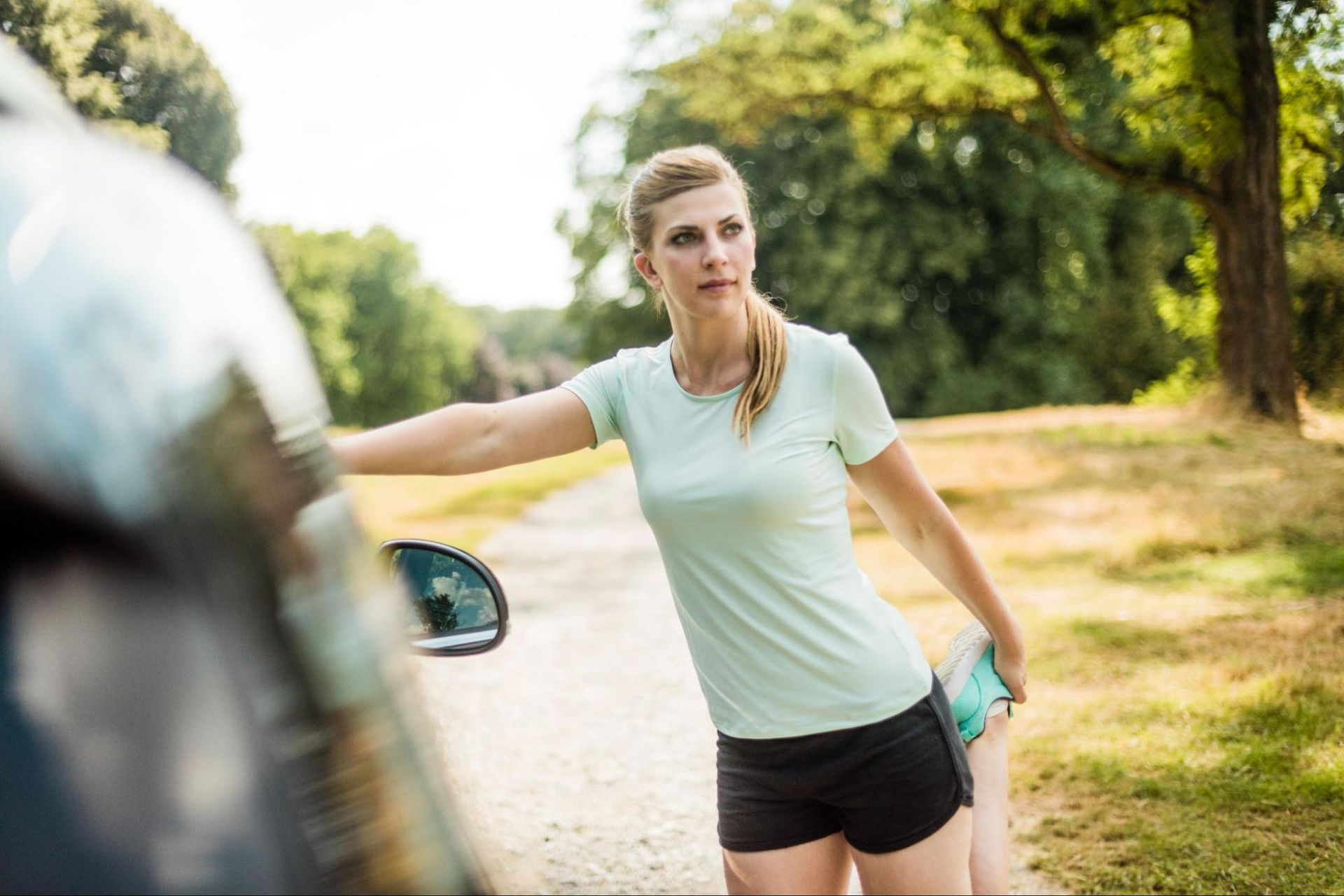 Woman stretching her leg and leaning against a car. 