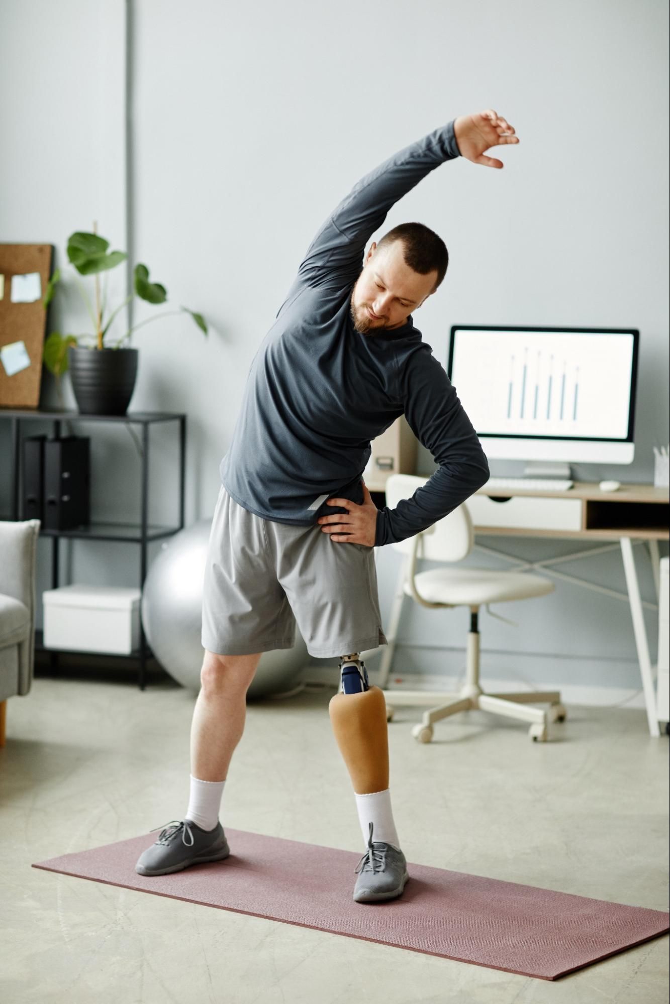A man with a prosthetic leg stretches on a yoga mat at home.