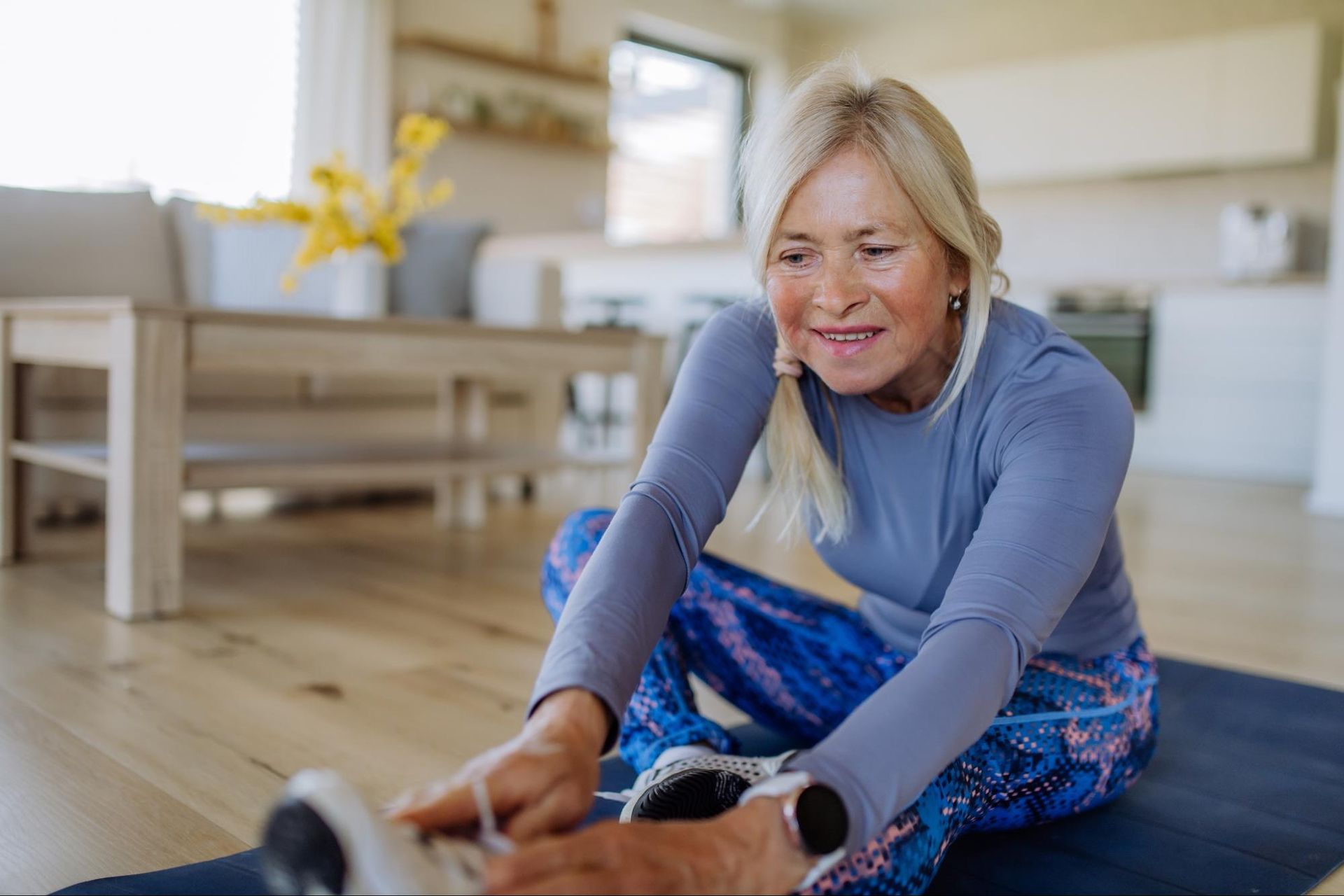 a senior woman in exercise gear stretches in her home.