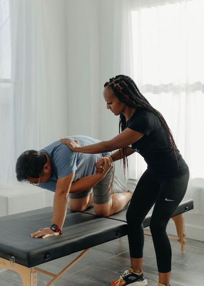 Physical therapist assists a person in exercise. Therapist stands to the side, holding the person's arm and back for support.