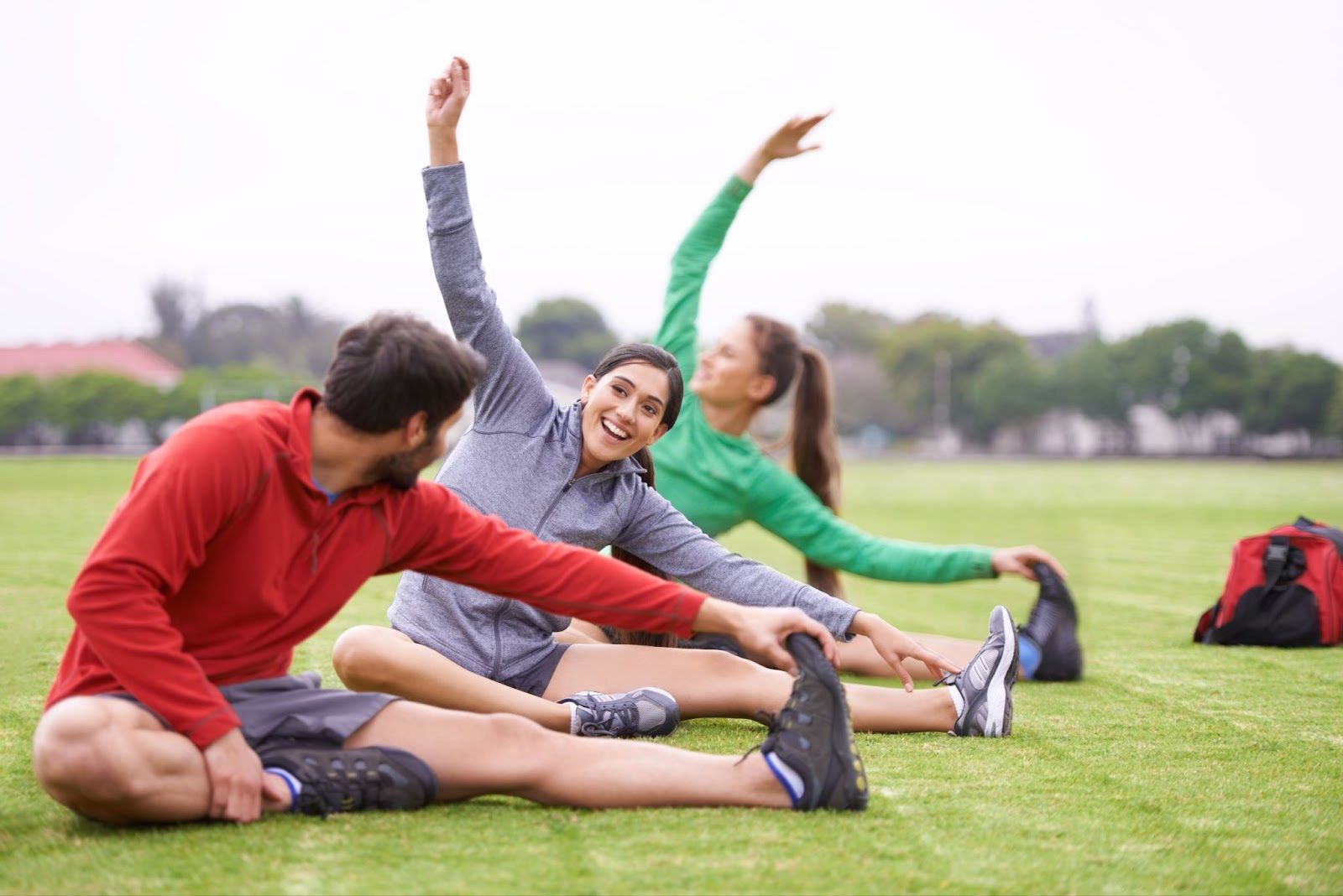Three people stretching on a soccer field. 
