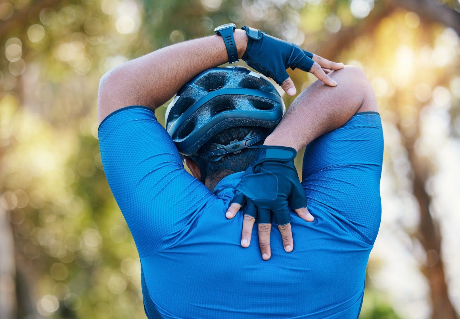 A cyclist wearing blue attire stretches his arms amidst nature.
