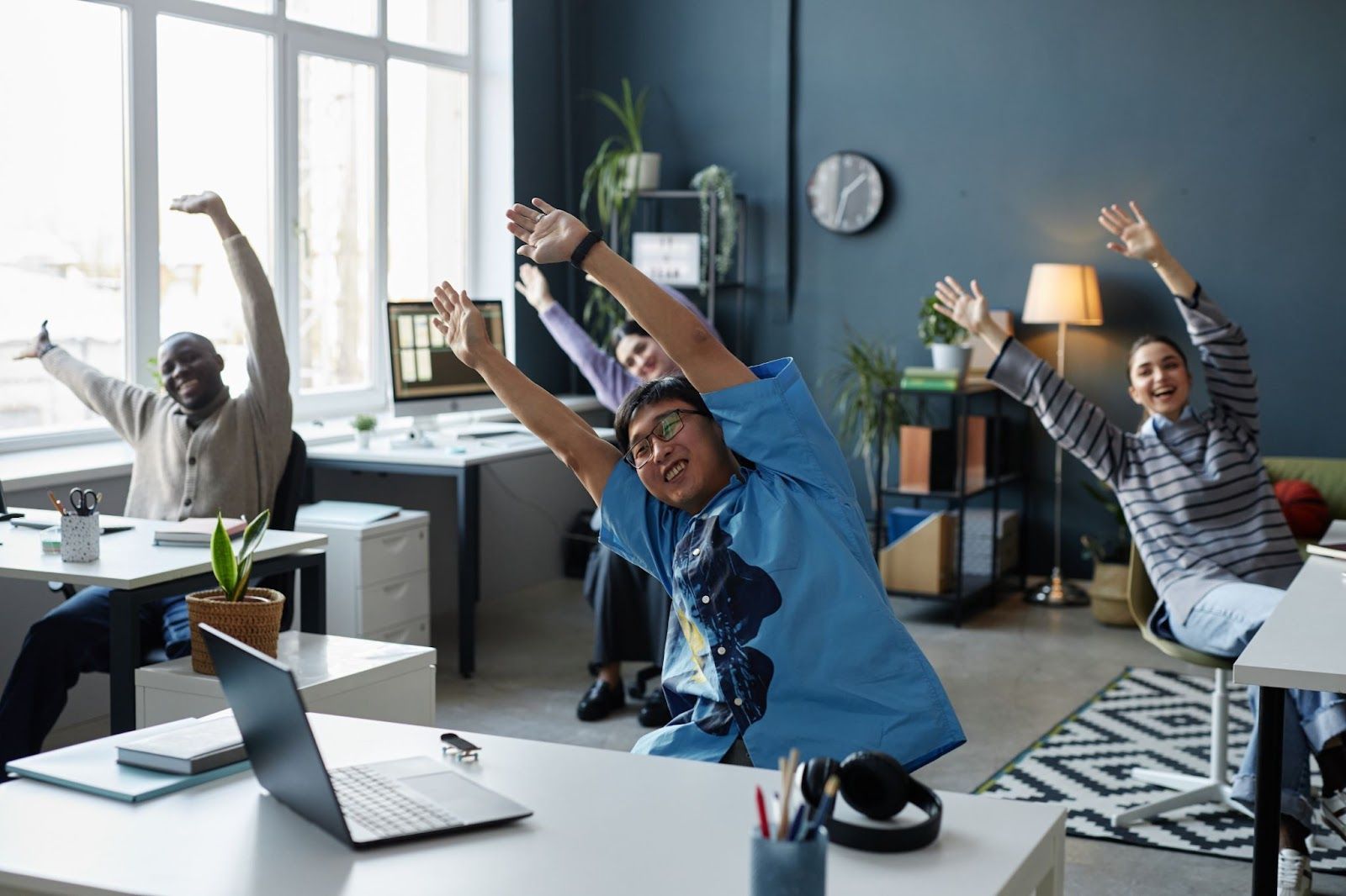 A diverse group of people are working together, enjoying stretching exercises, and having fun in the office.
