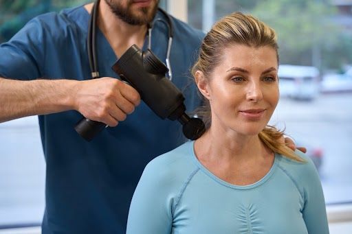 Medical professional using a massage gun on a woman. 