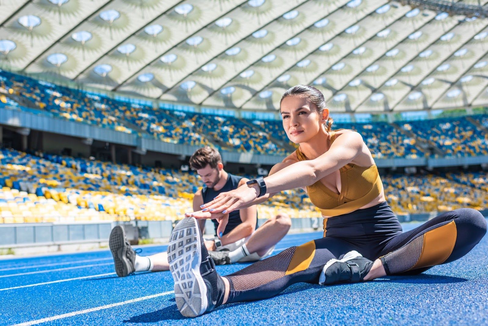 A man and a woman stretching inside a stadium.