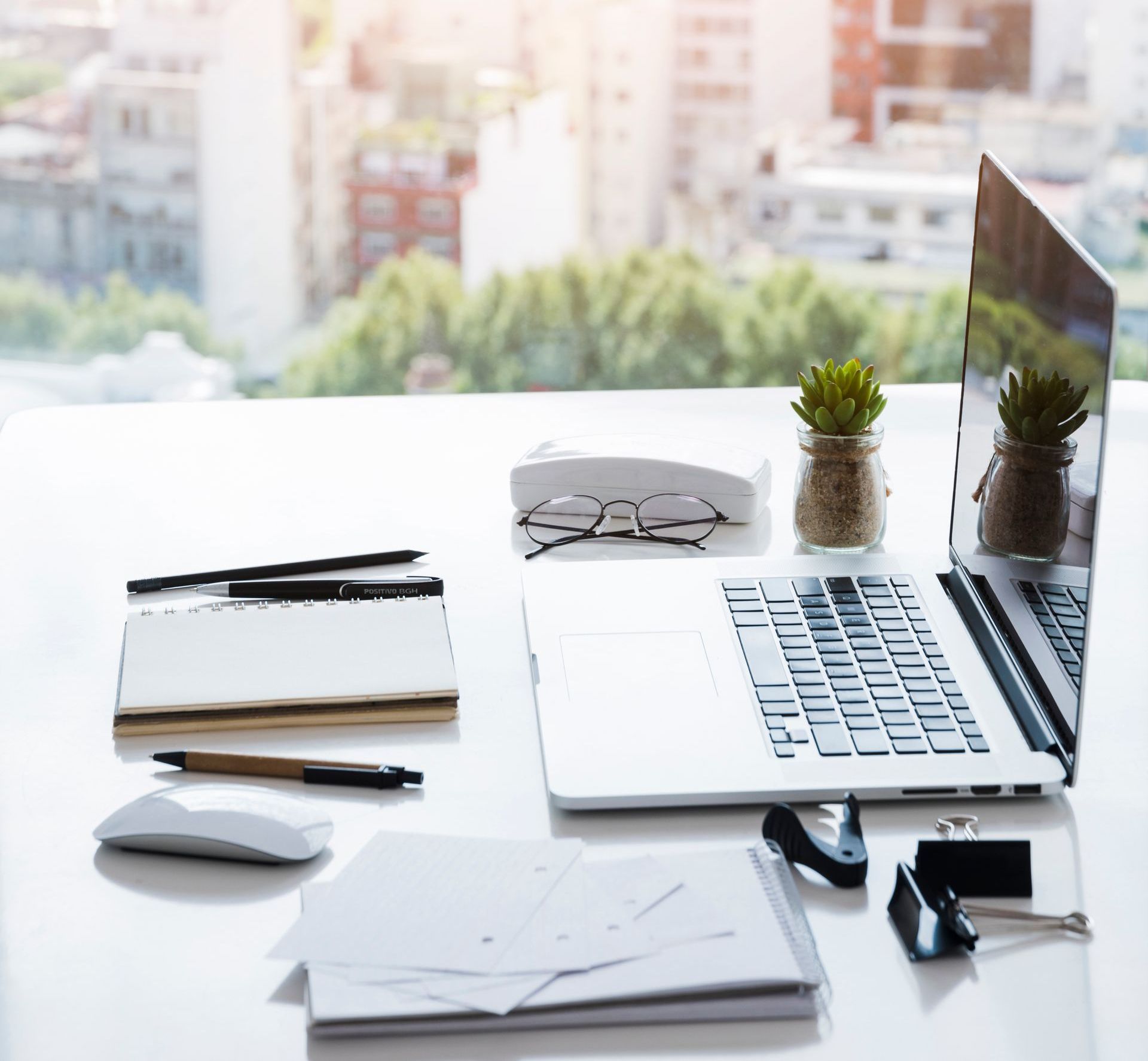 A woman in a white top and green skirt is standing in front of a wooden table.