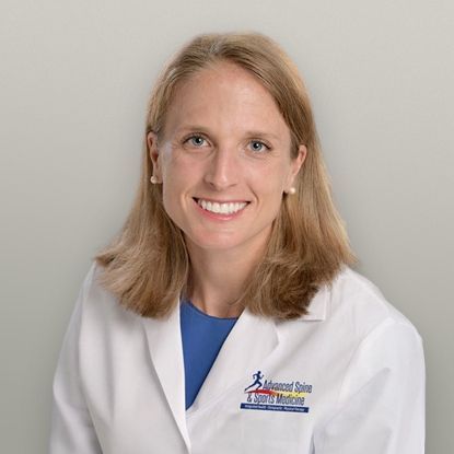 Woman wearing a white coat with logo, smiling, and looking at the viewer.