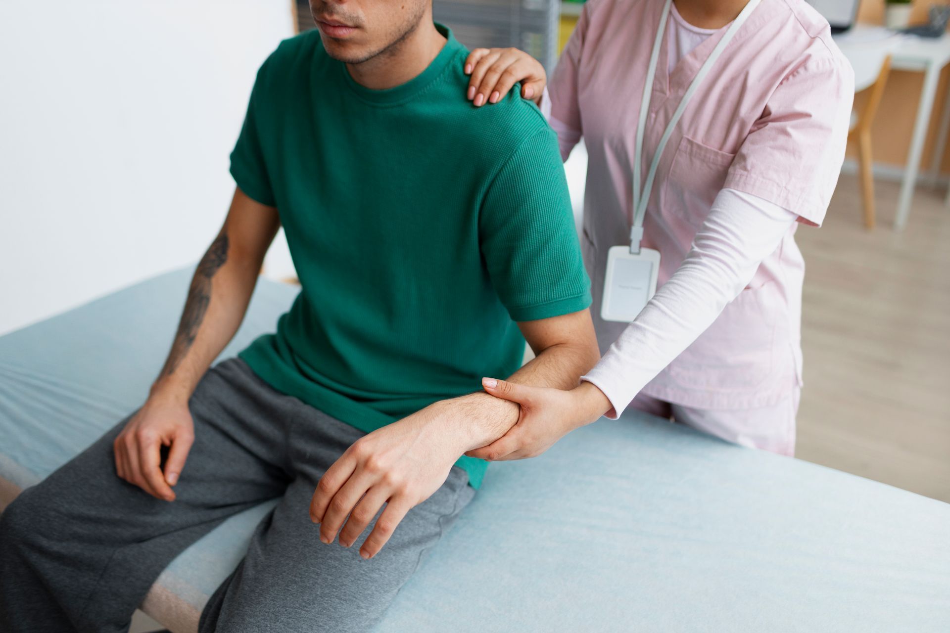 Person in green shirt receives arm support from a person in a pink uniform during physical therapy.