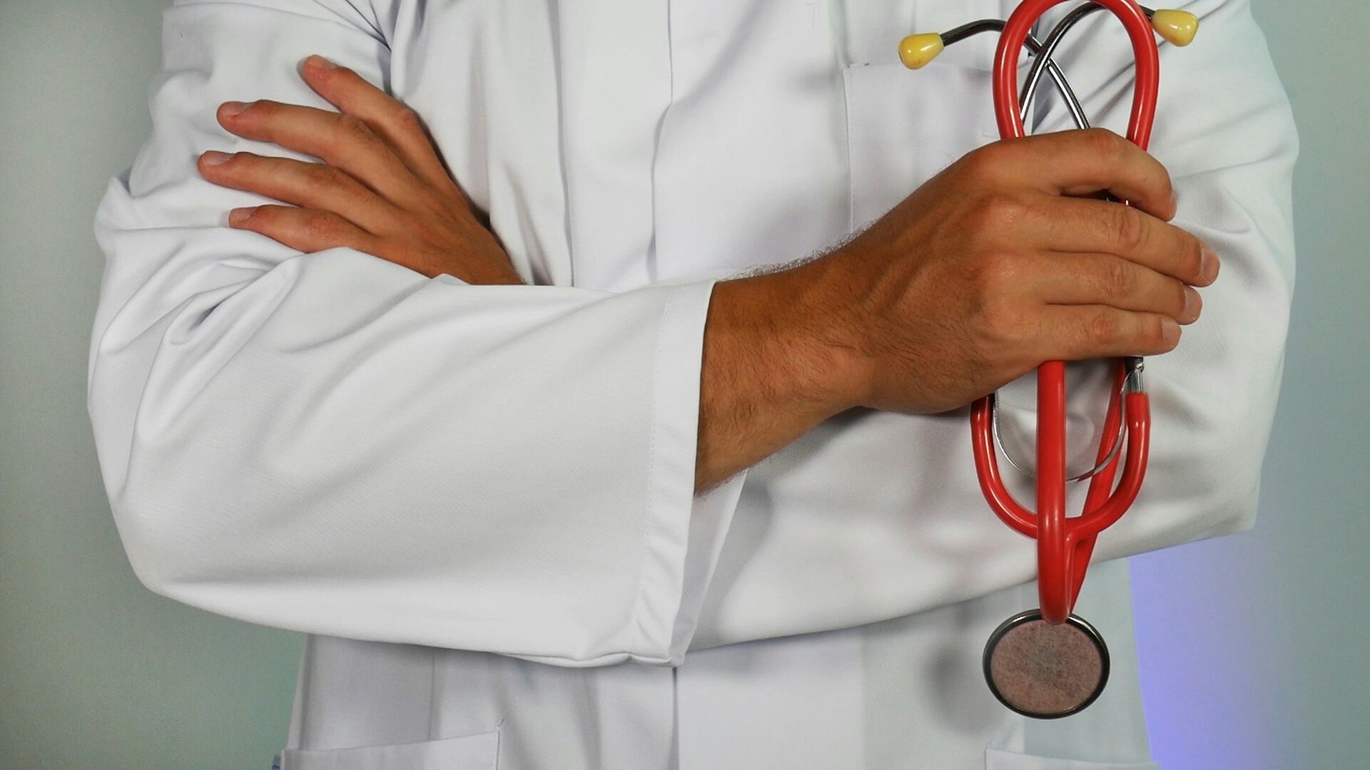 Doctor in white coat holding a red stethoscope, arms crossed.