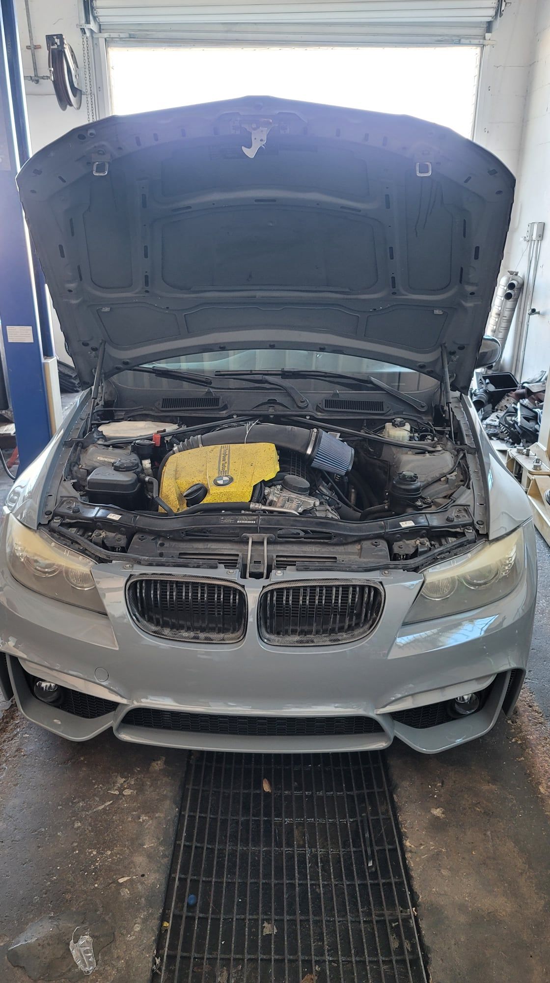 A silver bmw with the hood up in a garage.