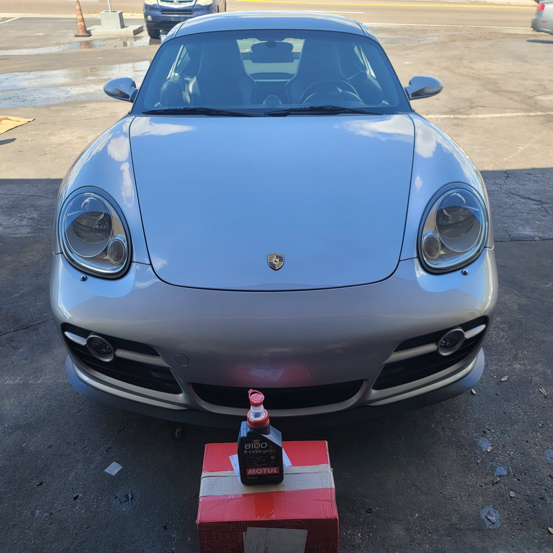 A silver sports car is parked next to a bottle of motor oil
