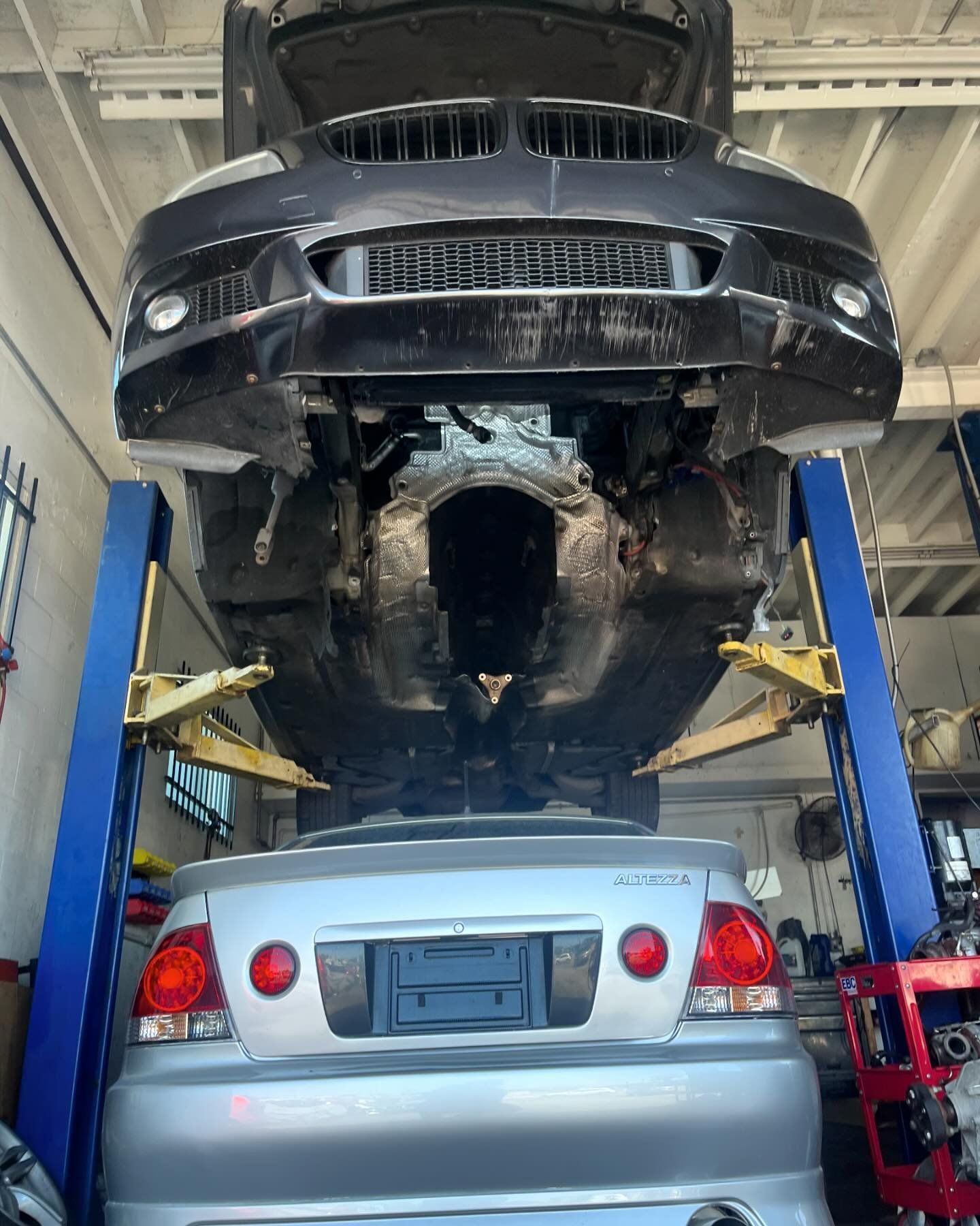 A car is sitting on a lift in a garage with the hood up.