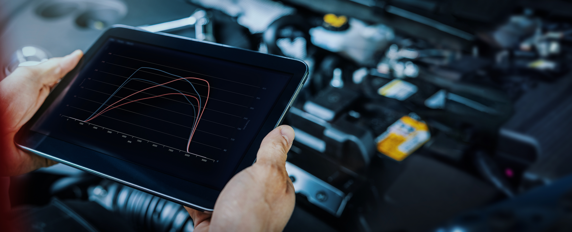 A person is holding a tablet in front of a car engine.