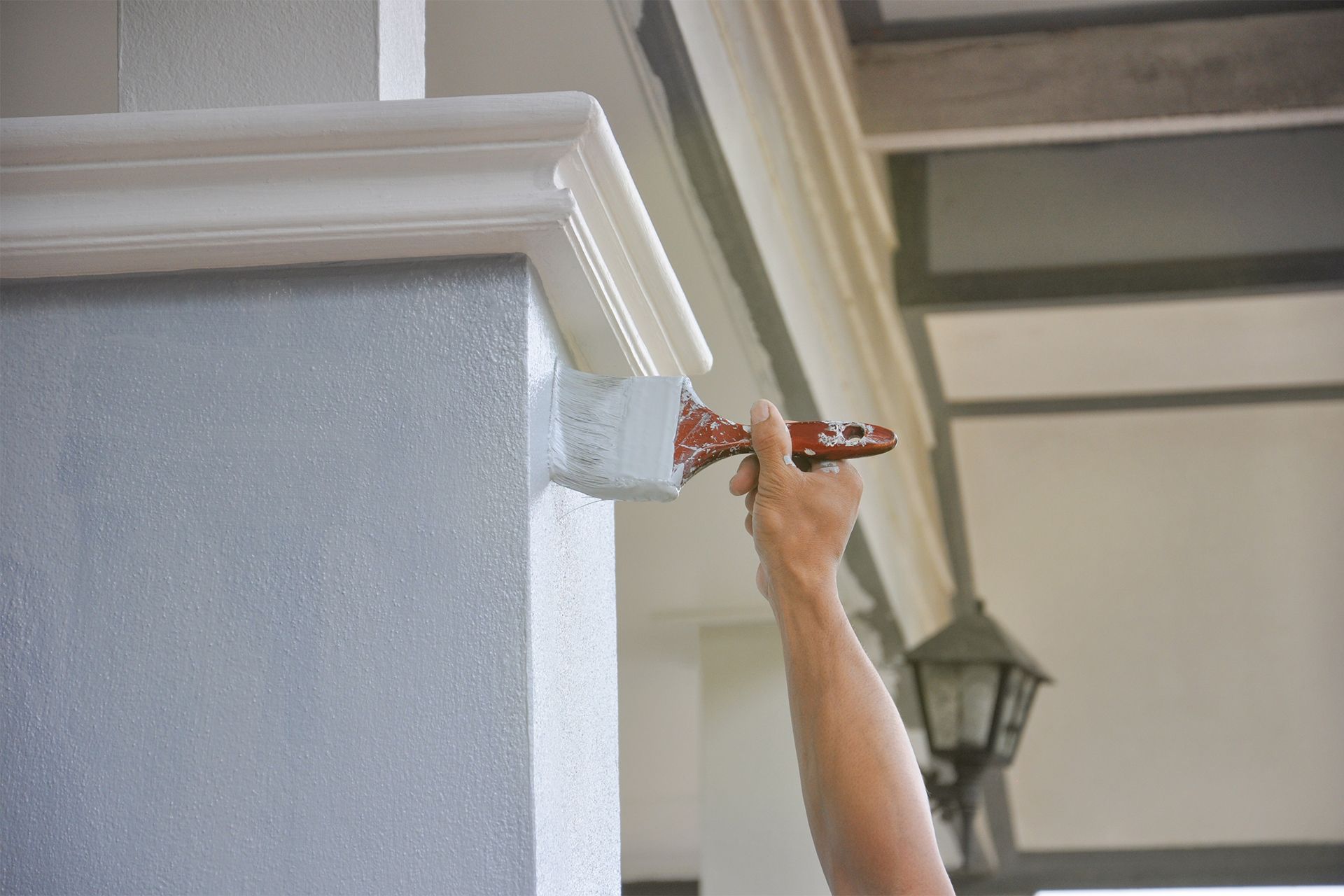 Person painting white trim on a light gray stucco wall with a paintbrush.