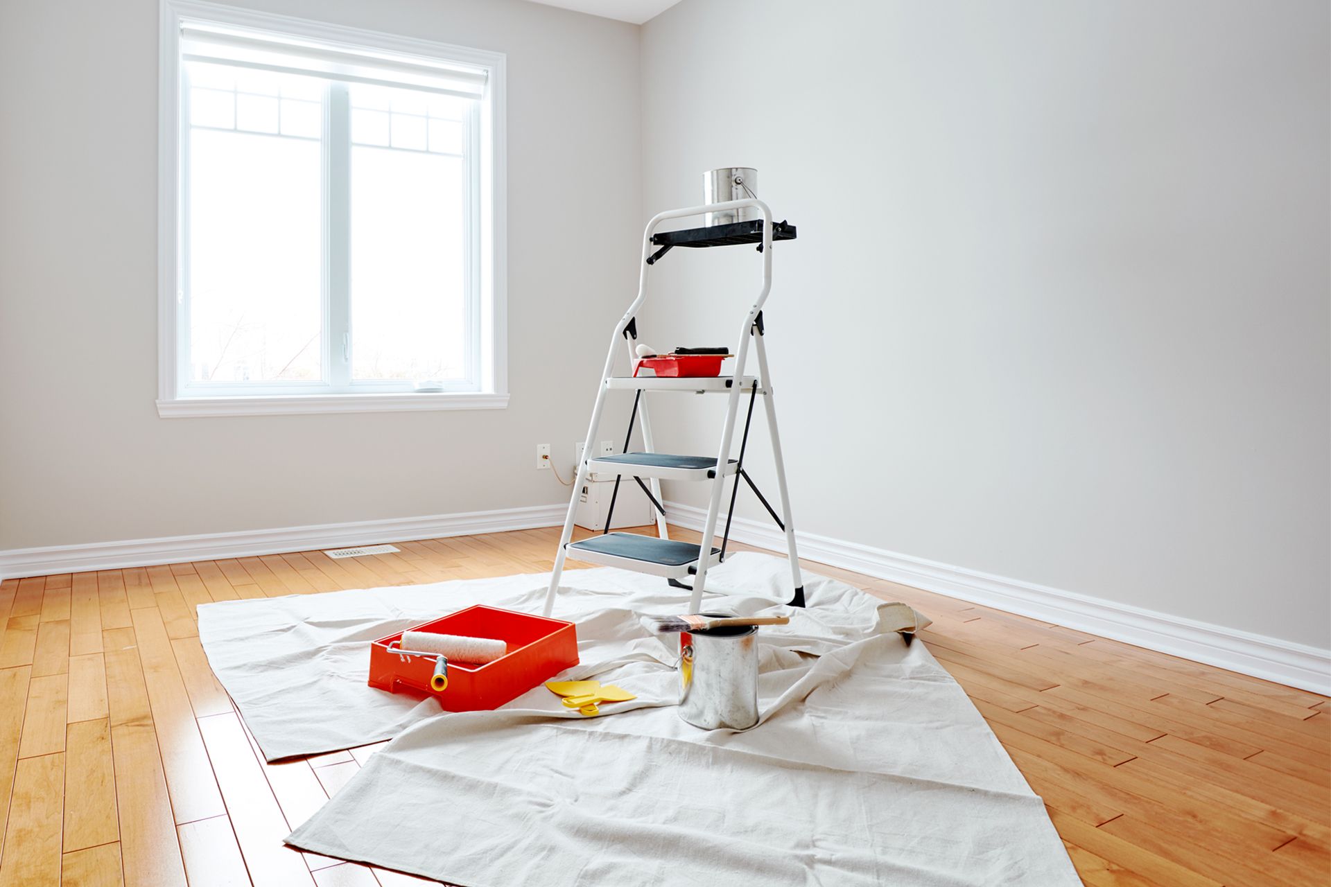 Room being painted with a ladder, paint can, and supplies on a drop cloth.