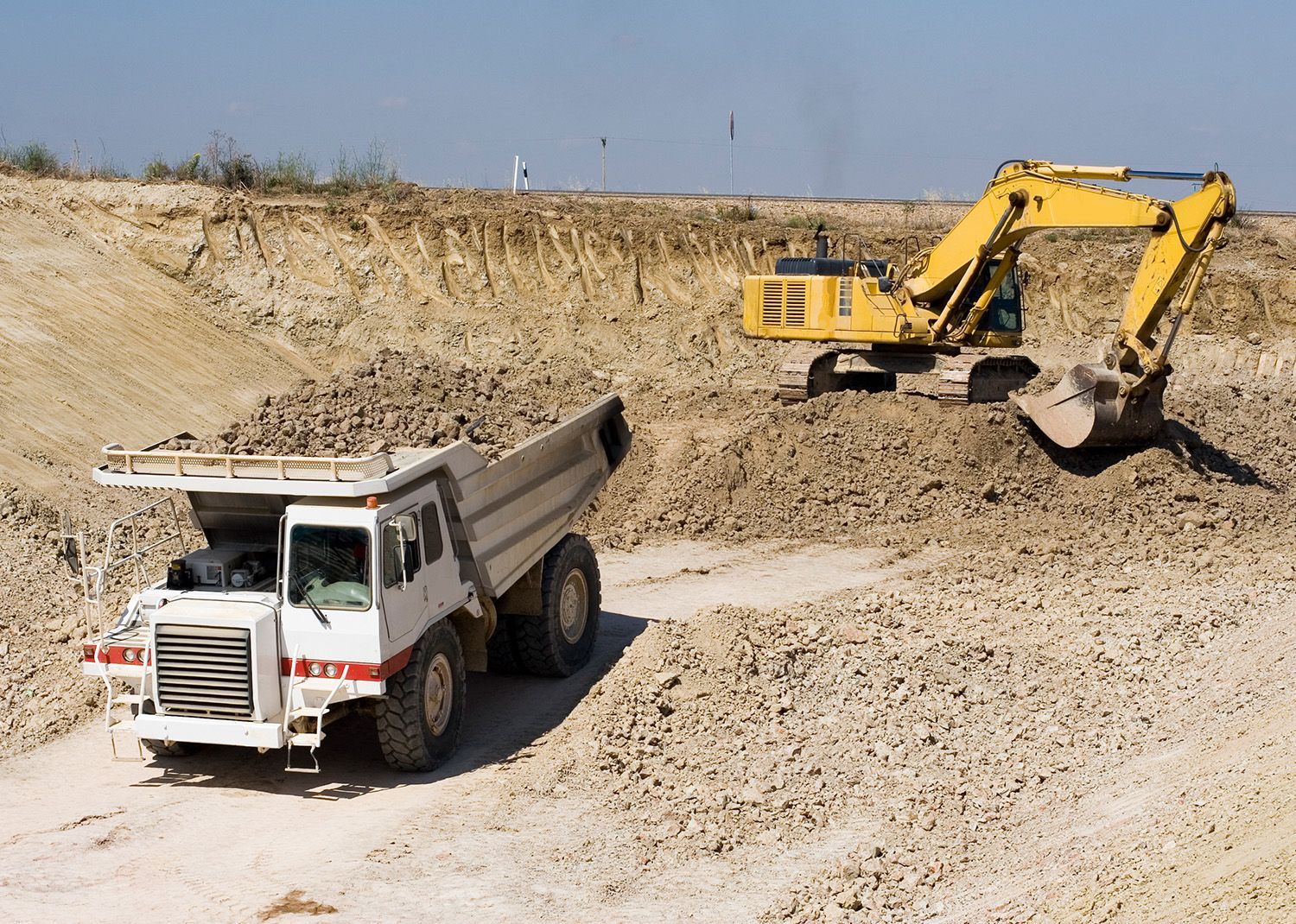 A yellow excavator loads dirt into a white dump truck at a construction site.