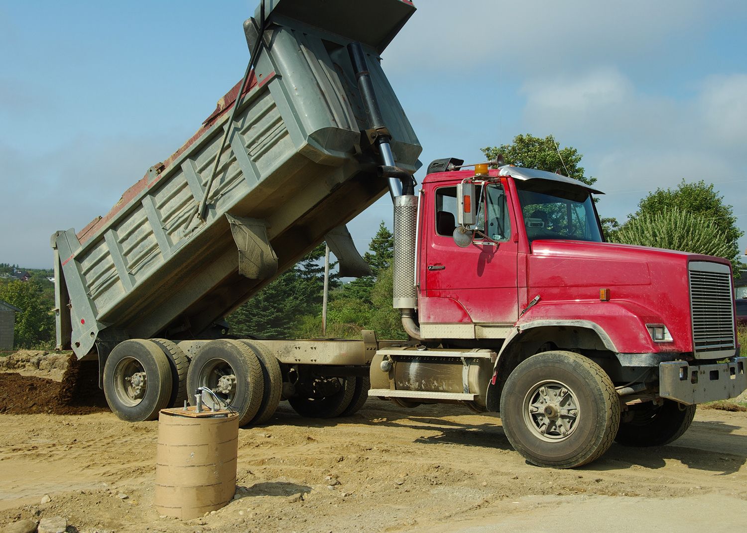 Red dump truck dumping dirt on a construction site; blue sky.