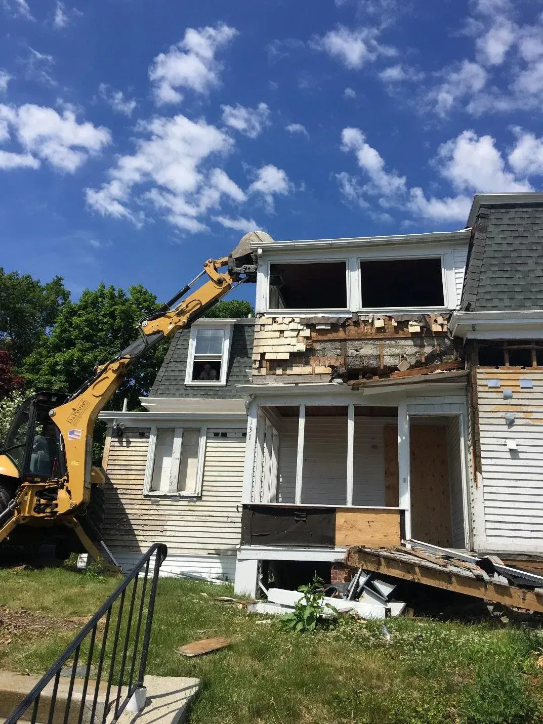 A yellow excavator demolishing a weathered, two-story house under a blue sky. A yellow excavator demolishing a weathered, two-story house under a blue sky.
