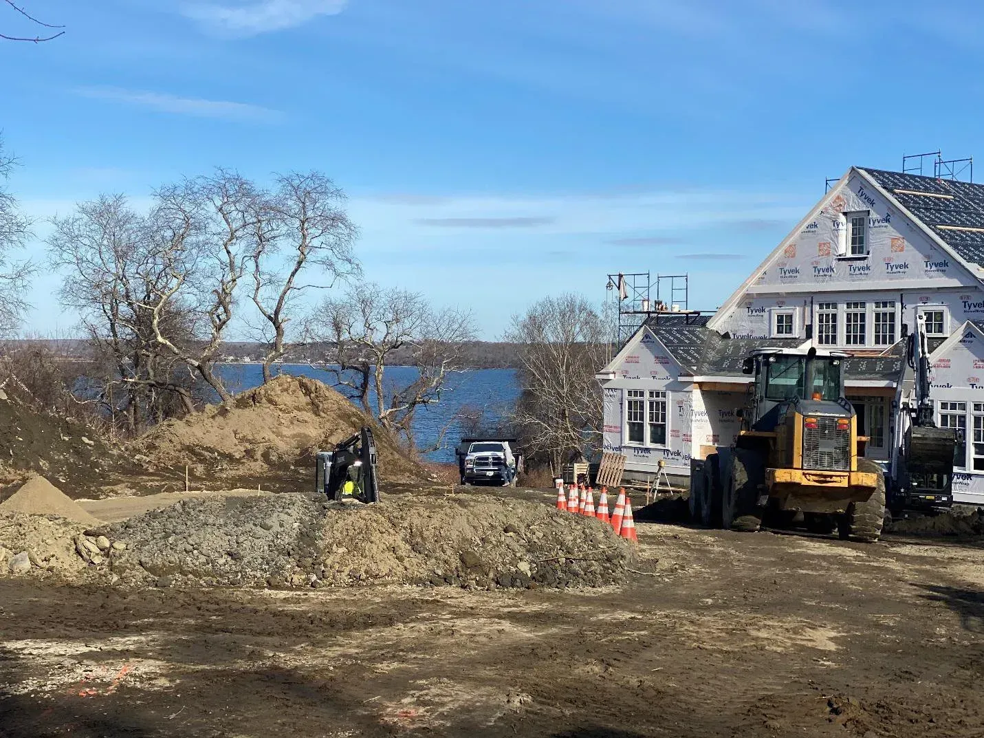 Construction site with building, earth moving equipment, and water view under blue sky. Construction site with building, earth moving equipment, and water view under blue sky.