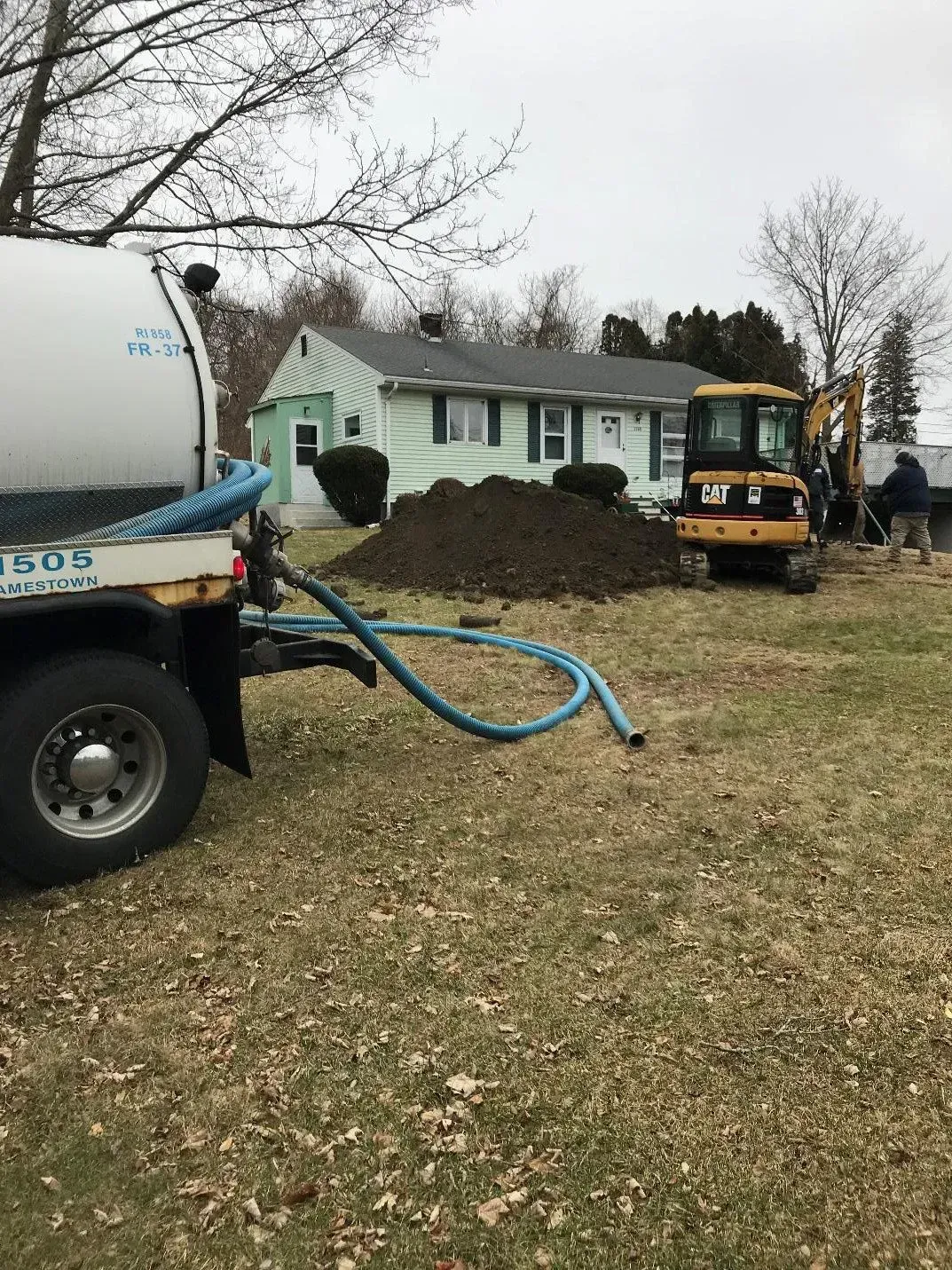 Septic tank service. Truck and mini-excavator near a house. Hose laid out, dirt pile visible. Cloudy day. Septic tank service. Truck and mini-excavator near a house. Hose laid out, dirt pile visible. Cloudy day.