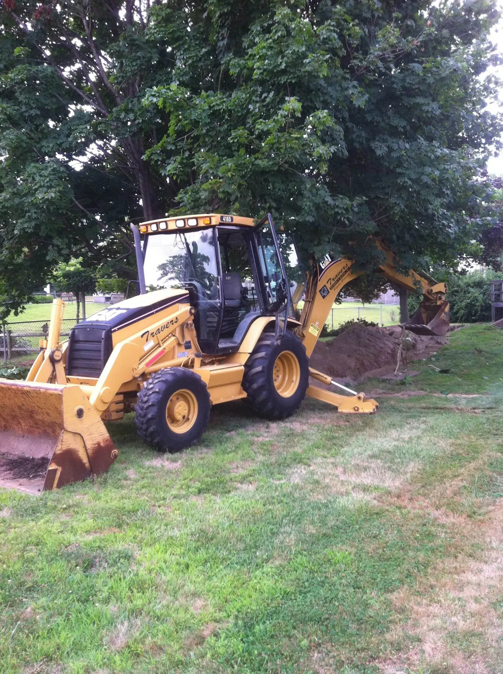 Yellow backhoe digging near a tree in a grassy yard. Yellow backhoe digging near a tree in a grassy yard.