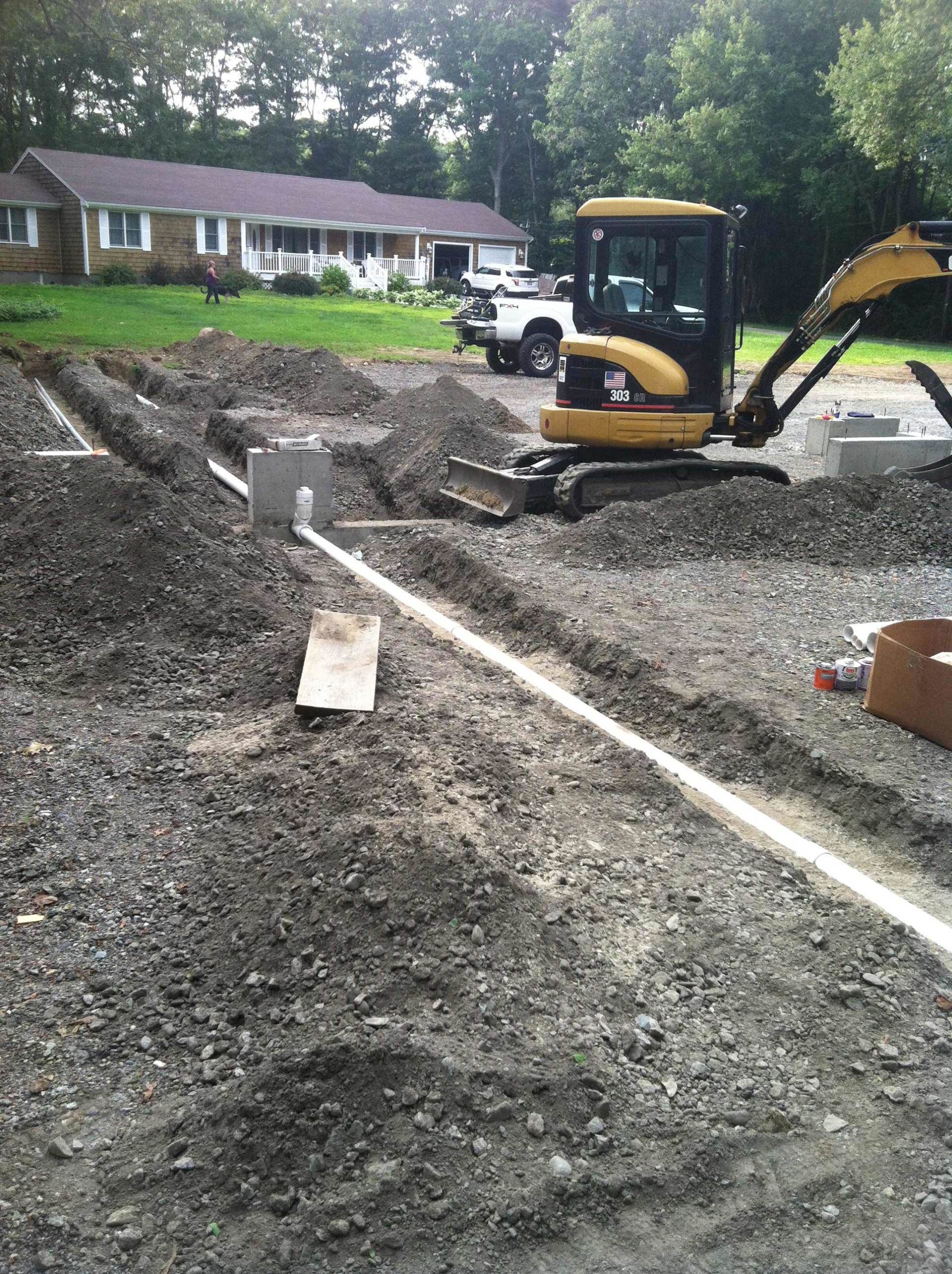 Construction site with mini excavator digging trenches, laying pipes in front of a residential house. Construction site with mini excavator digging trenches, laying pipes in front of a residential house.