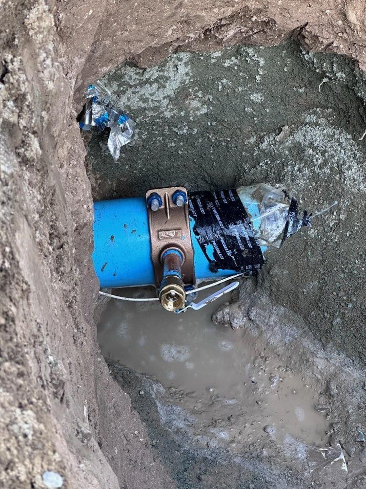 Blue pipe with a repair clamp in an excavated trench, filled with water and mud.