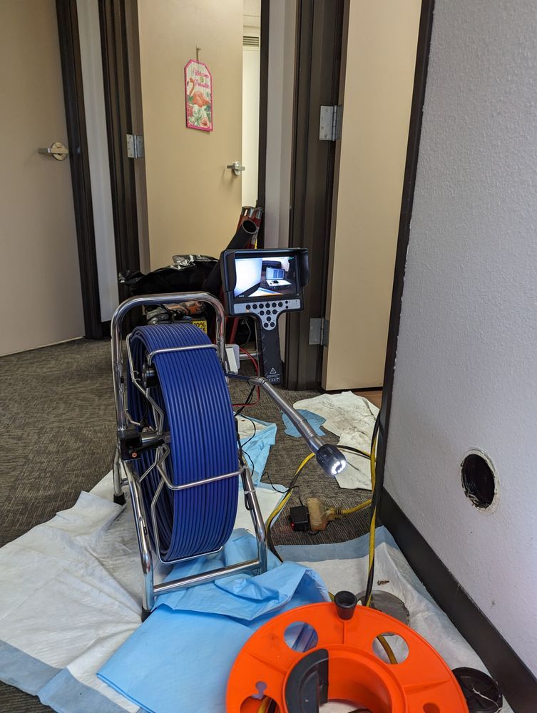 Plumbing camera setup in a doorway. Blue coiled cable, orange reel, screen showing camera view.