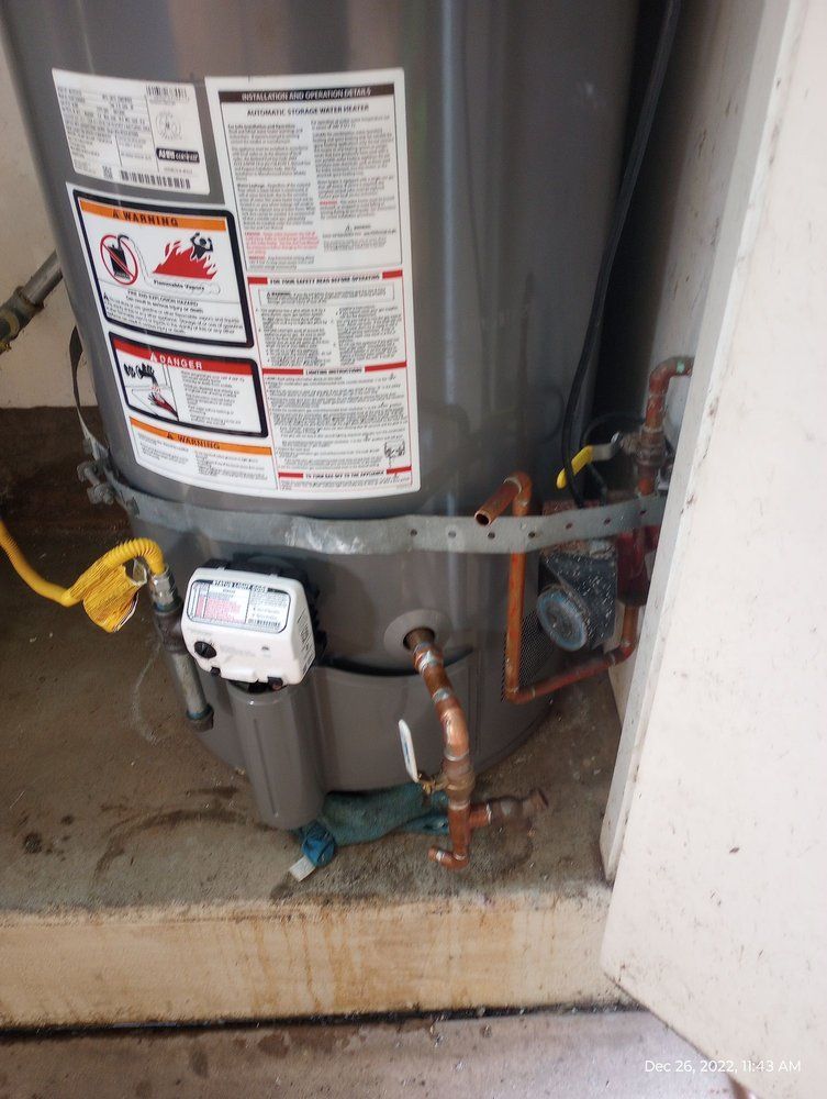 A water heater with copper pipes, connected to plumbing. Gray tank, white control box, yellow cable.