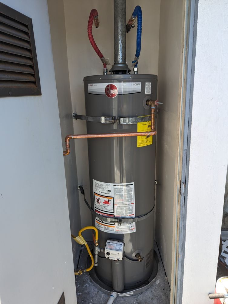 A Rheem water heater installed in an enclosed space with copper pipes and gas line.