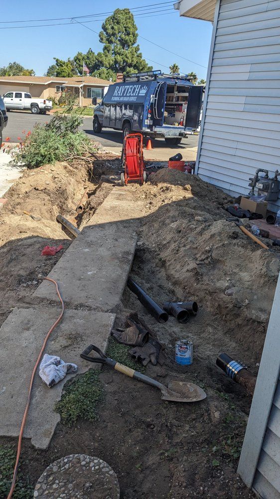 Trench dug for underground work next to a house; tools, pipes, and utility truck visible.