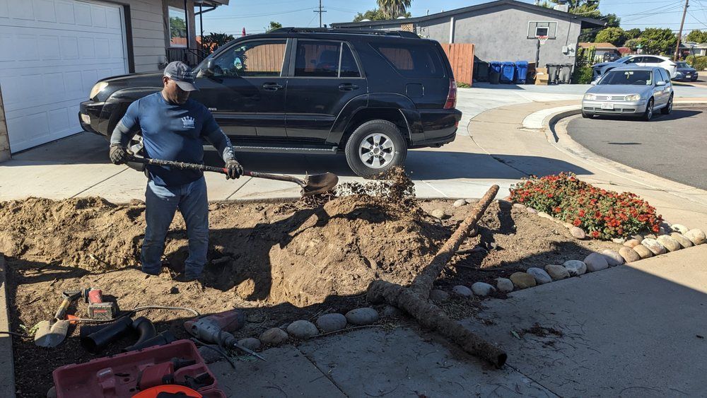 Man digging in a garden bed next to a driveway; a black SUV and a car are in the background.