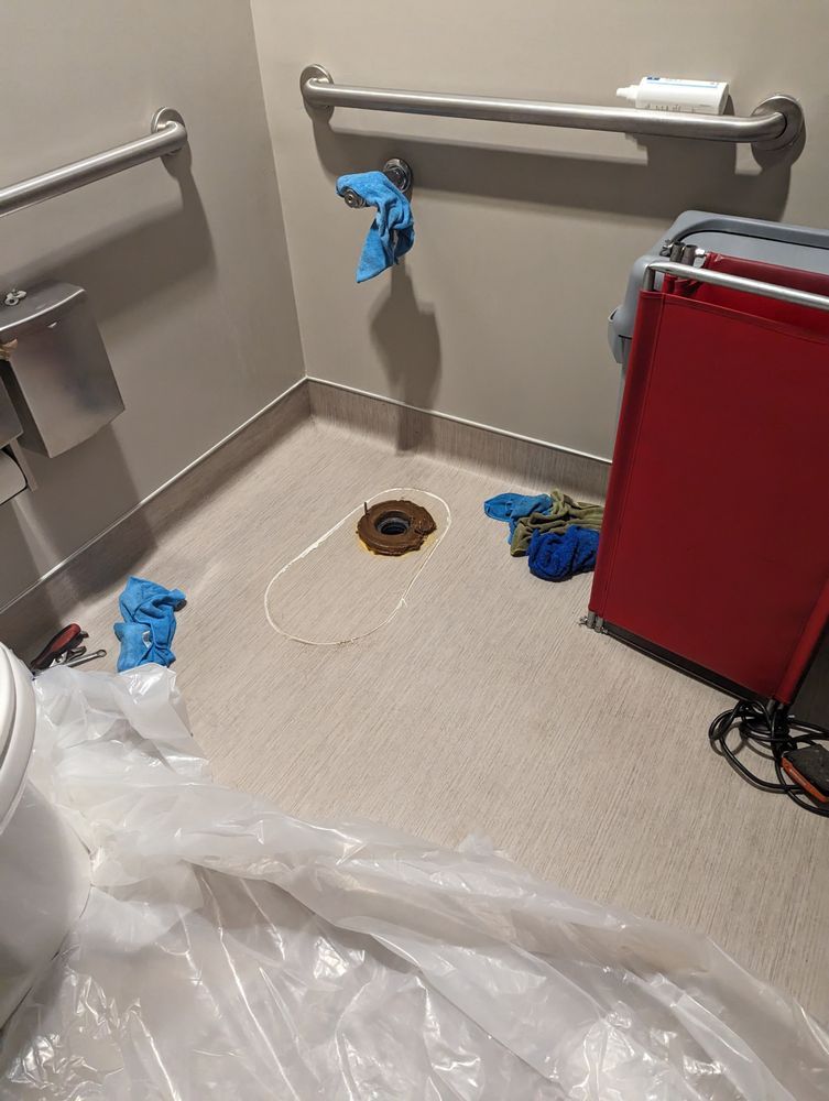 Bathroom with a removed toilet, repair in progress, with grab bars and protective plastic.