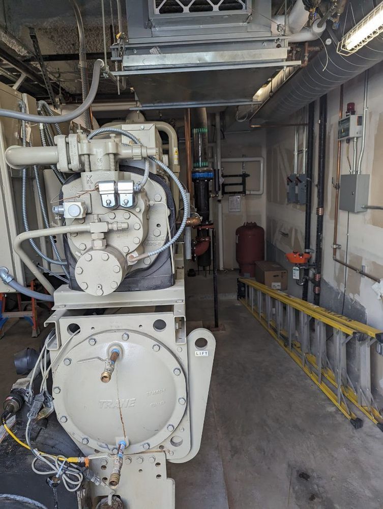 Machinery in a utility room; beige compressor, pipes, and a ladder are visible.